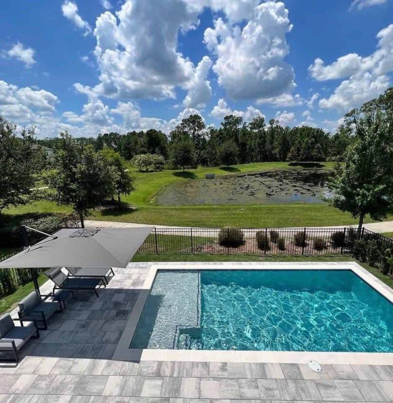 Poolside area with shade umbrella seating overlooking a green field and pond.