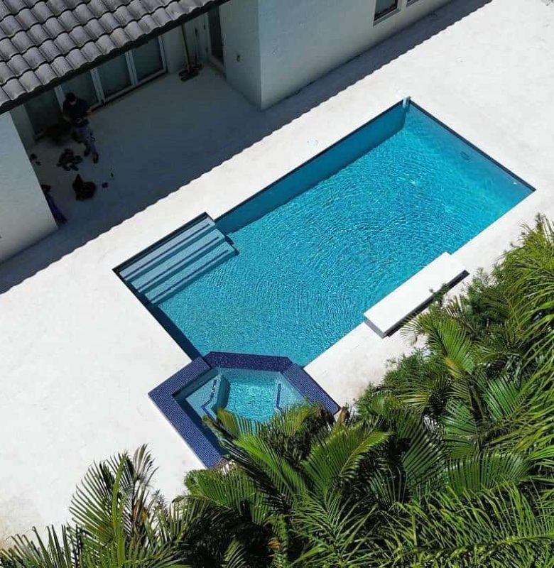 Aerial view of a modern backyard with a rectangular swimming pool and surrounding greenery.